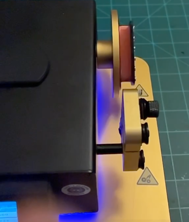 Programmable CNC pickup-winding machine in operation, gold-anodized fixture holding a copper-wire-loaded bobbin under blue ambient lighting